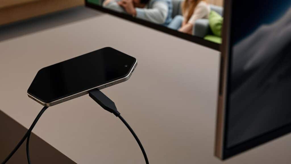 Celular conectado a uma TV via adaptador USB-C para HDMI, exibindo sua tela.